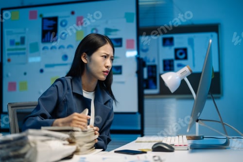 Preview: Young businesswoman works late under pressure, tired and stressed, surrounded by paperwork and techn