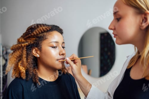 Preview: Caucasian blonde female master makes makeup for her dark skinned client in a beauty salon.