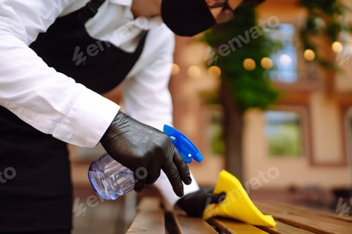 Preview: Disinfecting to prevent COVID-19. Waiter in protective face mask and gloves cleaning.
