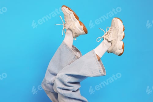 Preview: Woman wearing stylish sneakers on light blue background, closeup