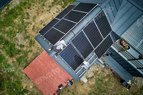 Preview: Electricians connecting cables while installing photovoltaic solar panels on roof of house.