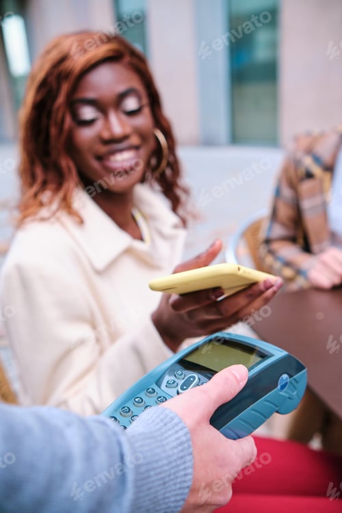 Preview: Woman smiling while making contactless payment with a mobile phone at a coffee shop.
