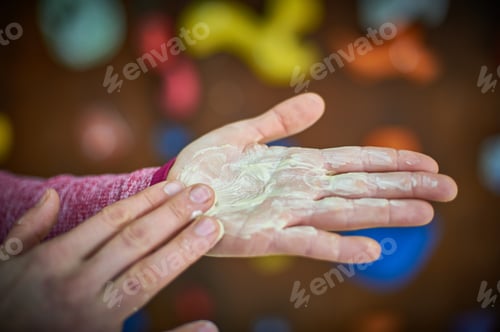 Preview: Climber applying chalk to hands before bouldering session at indoor climbing gym during afternoon