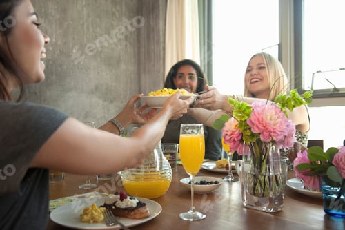 Preview: Group of friends having meal at table, young woman passing plate to friend