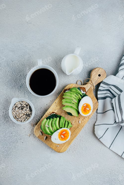 Preview: Delicious avocado toast on rye grain bread board, cup of black coffee on concrete background