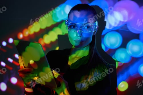 Preview: Beautiful young woman in futuristic glasses using digital tablet against colorful background