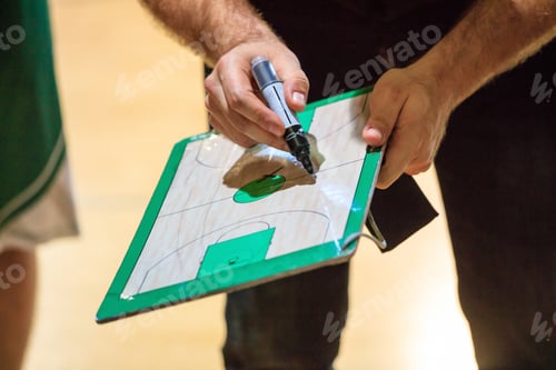Preview: Basketball coach holds a clipboard and with a marker explain the tactic of the game to a player.