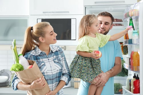 Preview: Happy family with products near refrigerator in kitchen