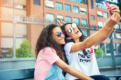 Preview: Giggling friends taking photos on bench