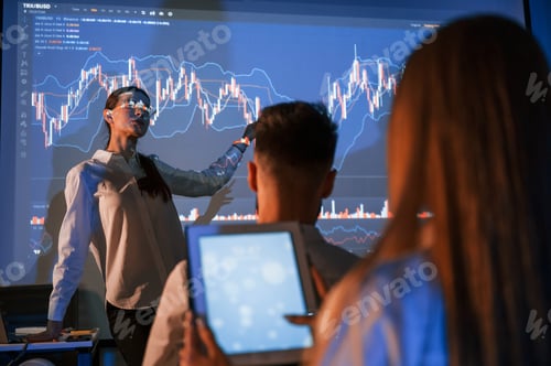 Preview: Graphs on projector. Female leader talking to employees in office of stock exchange company
