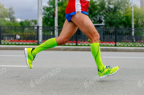 Preview: close-up legs runner athlete running marathon in city in green compression socks, sports summer race