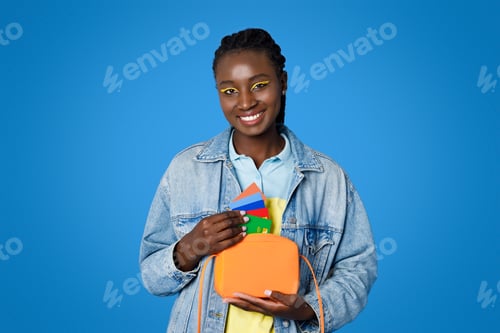 Preview: Positive stylish young black woman holding purse and bank cards