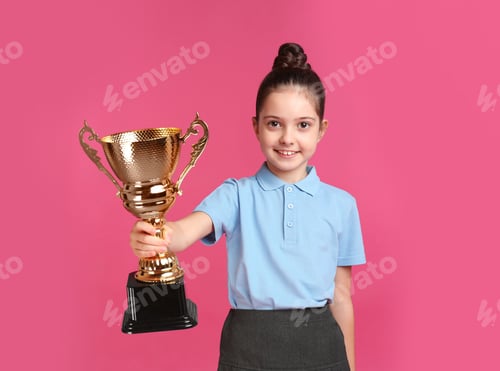 Preview: Happy girl in school uniform with golden winning cup on pink background. Space for text