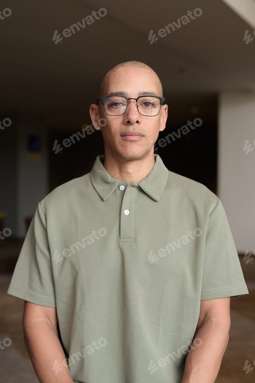 Preview: Bald Hispanic man in hotel lobby with eyeglasses, stylish confident portrait in casual setting