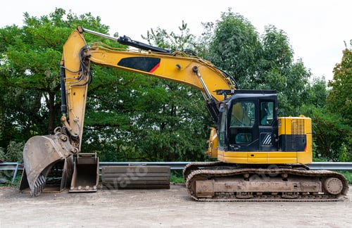 Preview: A large excavator in yellow color visible from the profile with a lowered bucket.