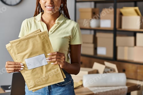 Preview: cropped view of young african american woman with braces holding post packets during work, delivery