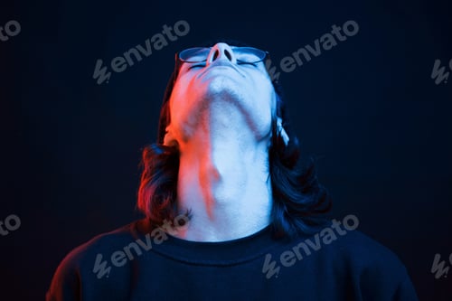 Preview: Putting head up. Studio shot in dark studio with neon light. Portrait of serious man