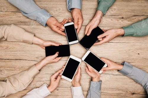 Preview: Top view of business people holding smartphones at wooden table, cropped view