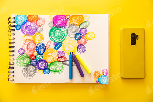 Preview: Closeup shot of a phone and markers on a paper with colorful swirls