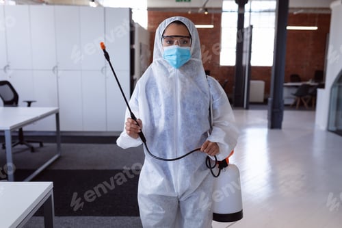 Preview: Portrait of cleaner wearing ppe suit, glasses and mask disinfecting office workspace