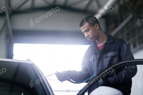 Preview: A focused mechanic attentively services a car in a welllit garage.