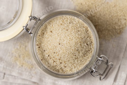 Preview: Jar of raw uncooked fonio seeds on gray napkin top view. African pseudocereal. Healthy food concept