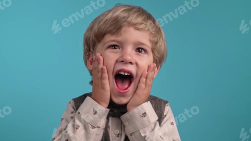 Preview: Amazed european little boy shocked, saying WOW.Handsome kid surprised to camera on blue background