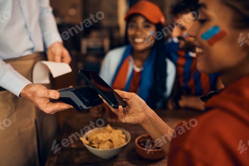 Preview: Close up of sports fan paying with her cell phone during the world cup in bar.