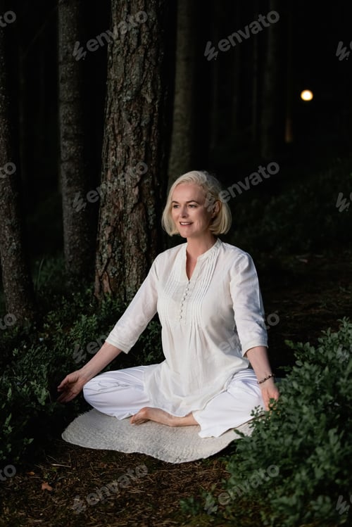 Preview: middle aged woman doing yoga outdoors in forest
