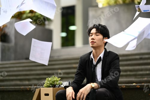 Preview: Desperate businessman sitting on the stairs of building with falling paperwork.
