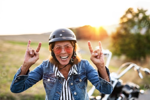 Preview: A cheerful senior woman traveller with motorbike in countryside at sunset.