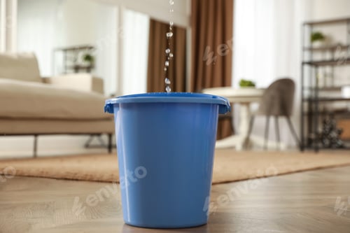 Preview: Bucket collecting water from ceiling in living room. Leaking roof