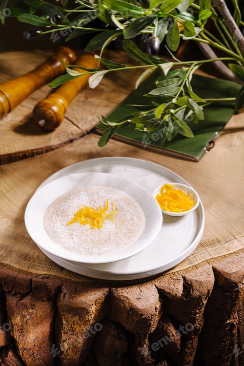 Preview: Bowl of oatmeal or rice porridge with coconut flakes and orange zest on a wooden table.