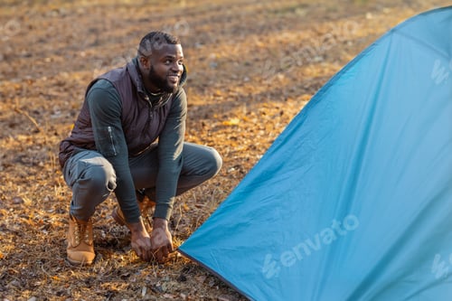 Preview: Black guy setting up blue tent in forest