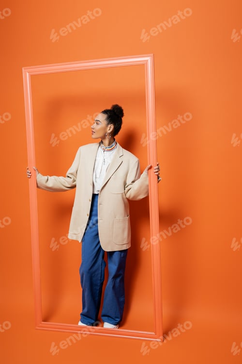 Preview: attractive young woman in street outfit with bun and vivid makeup standing inside of framework