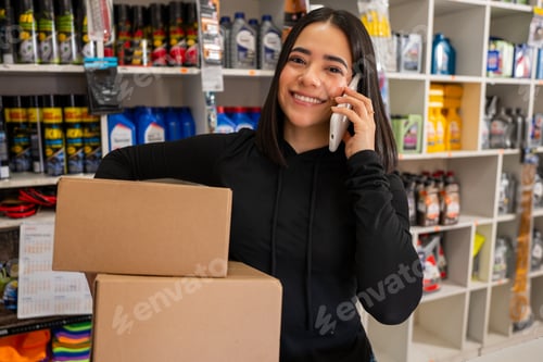 Preview: Smiling woman holding boxes and talking on a cell phone inside a store