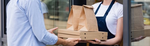 Preview: Panoramic shot of man receiving pizza boxes and paper bags for takeaway from waitress near window of