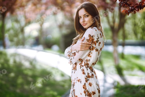 Preview: Beautiful young woman near tblooming spring tree. Attractive girl enjoying her time outside in park.