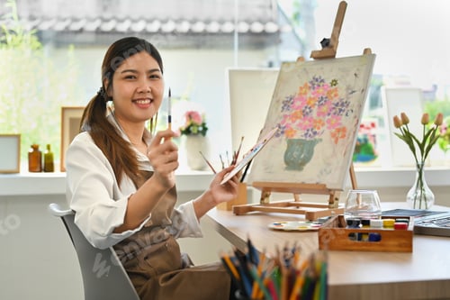 Preview: Attractive female artist painting with watercolor on canvas in art workshop.