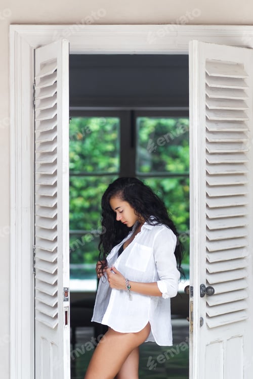 Preview: Beautiful woman with long black hair posing near white door in black lingerie. Morning mood