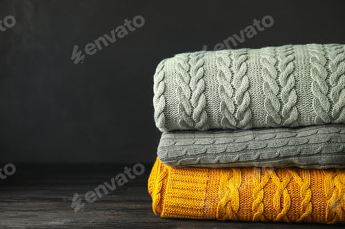 Preview: Stack of soft plaids on black wooden table, closeup. Space for text