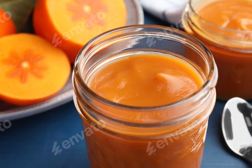 Preview: Delicious persimmon jam in glass jar and fresh fruits on blue table, closeup
