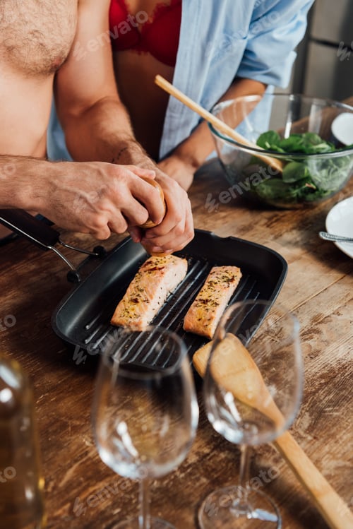 Preview: cropped view of sexy girl and shirtless man seasoning fish in frying pan