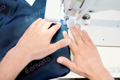 Preview: Human hands holding dark blue fabric while sewing by machine