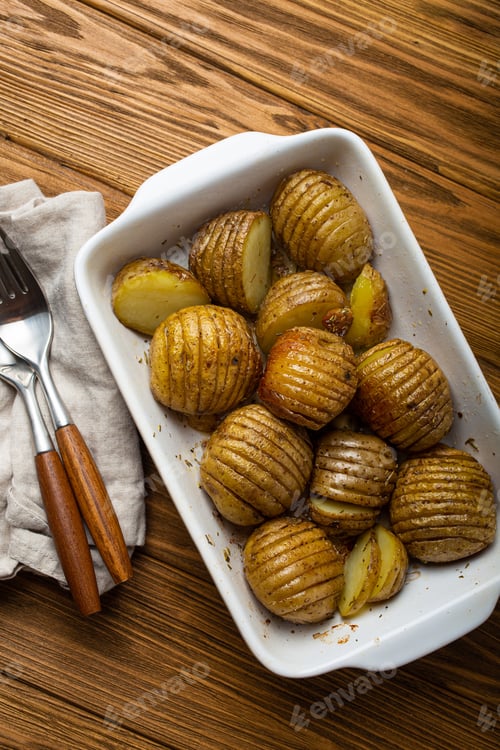 Preview: Hasselback baked potatoes in white ceramic casserole dish on wooden rustic table background