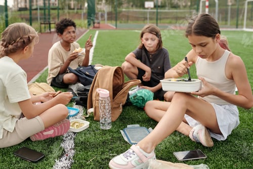 Preview: Group of hungry intercultural schoolchildren having lunch on stadium