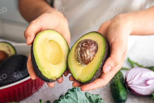 Preview: Avocado halves in a female hand in the kitchen.