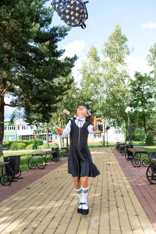 Preview: Cheerful funny girl with toothless smile in school uniform with white bows in school yard tosses the