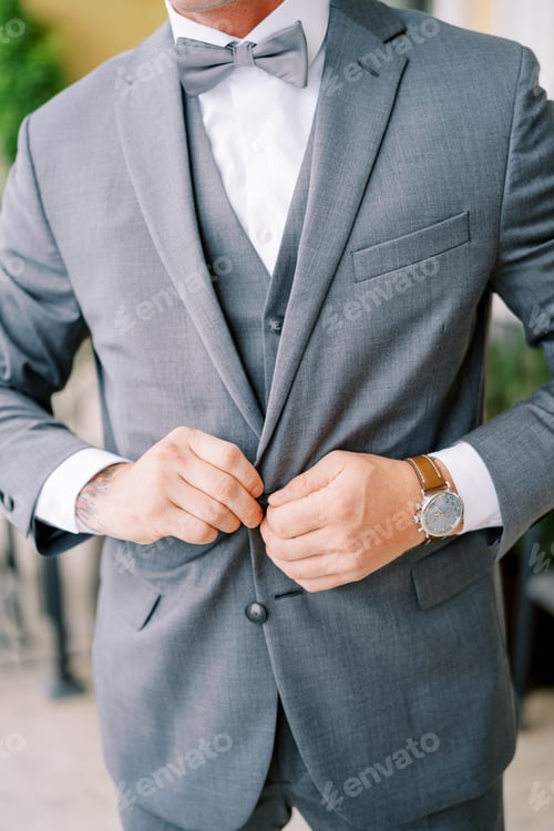 Preview: Groom fastens the buttons of his jacket. Cropped. Faceless