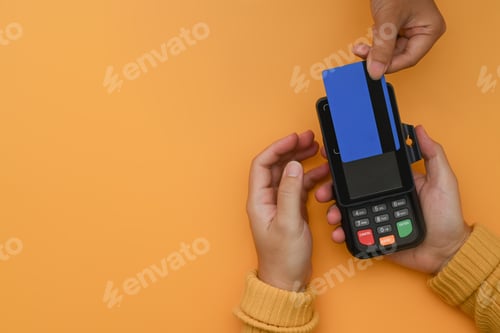 Preview: Overhead view of customer paying with cashless technology with credit card on yellow background